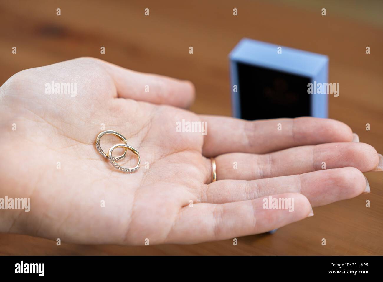 Hand, die raffinierte Goldreifen mit winzigen eingebetteten Kristallen hält, mit einem unscharfen Schmuckkästchen im Hintergrund, was eine durchdachte Geschenkidee symbolisiert Stockfoto
