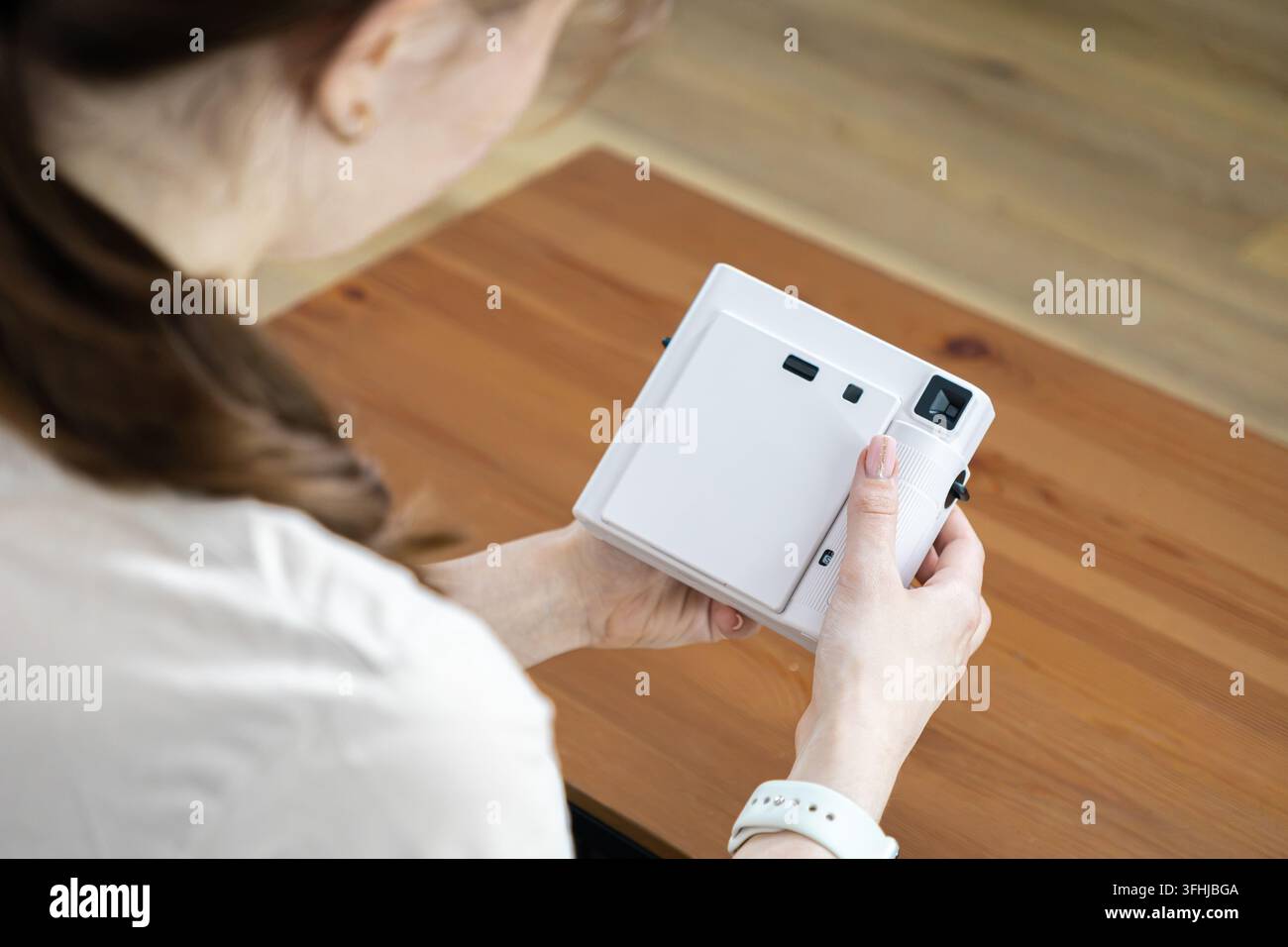 Eine Person bedient eine kompakte Sofortbildkamera über einer natürlichen Holzoberfläche und verkörpert Themen der Nostalgie, Freizeitaktivität und künstlerischen Ausdrucks Stockfoto