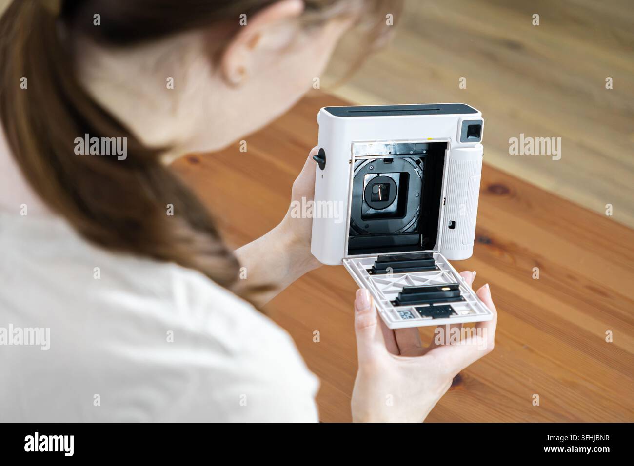 Eine Person setzt vorsichtig eine Kassette in eine tragbare Sofortbildkamera ein und betont dabei das taktile Erlebnis und die technischen Details, die mit der Vorbereitung verbunden sind Stockfoto