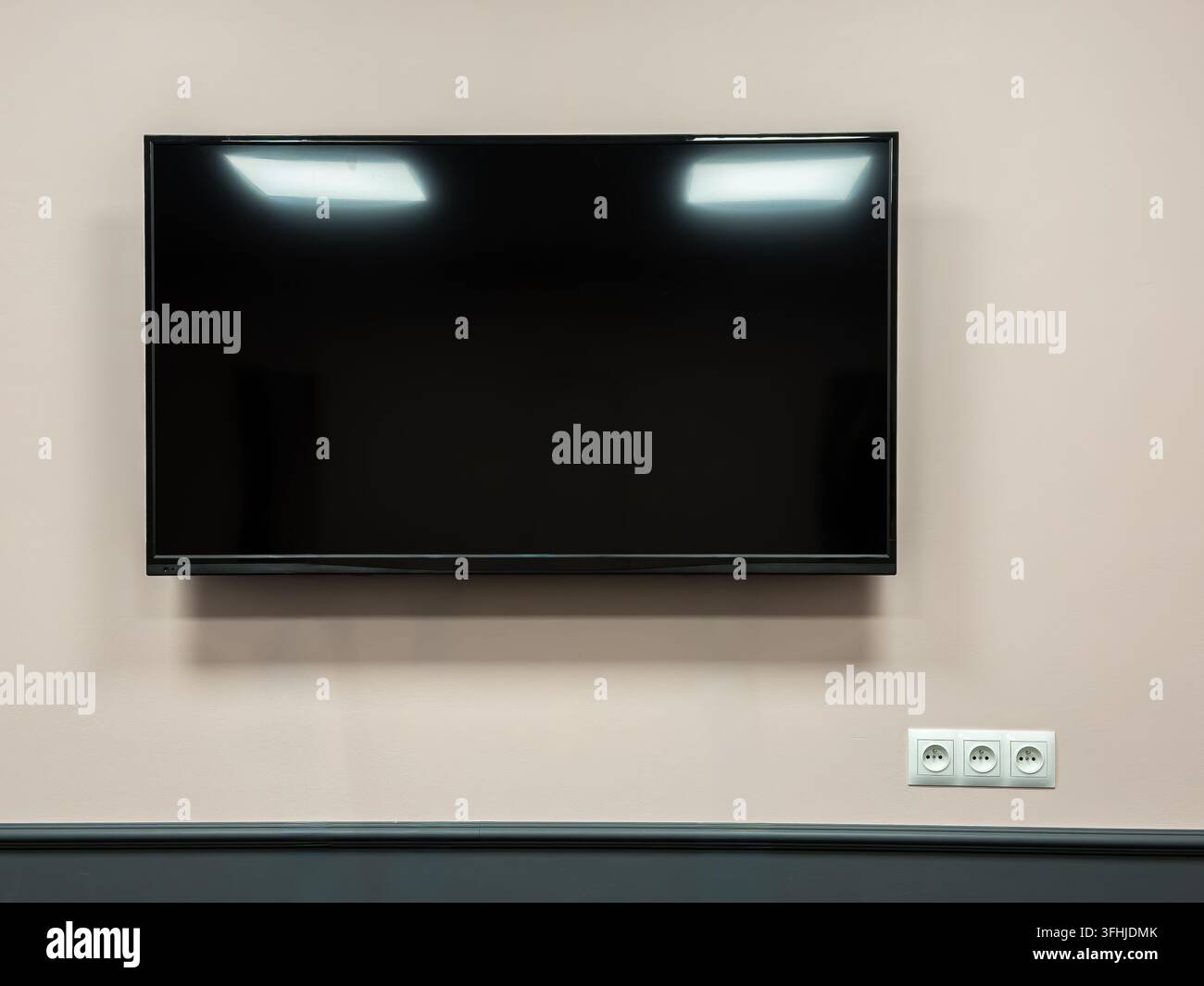 Ein leerer Flachbildschirm hängt über elektrischen Steckdosen an einer hellen Wand und schafft einen vielseitigen Hintergrund für digitale Anzeige-Setup in einem stilvollen Co Stockfoto