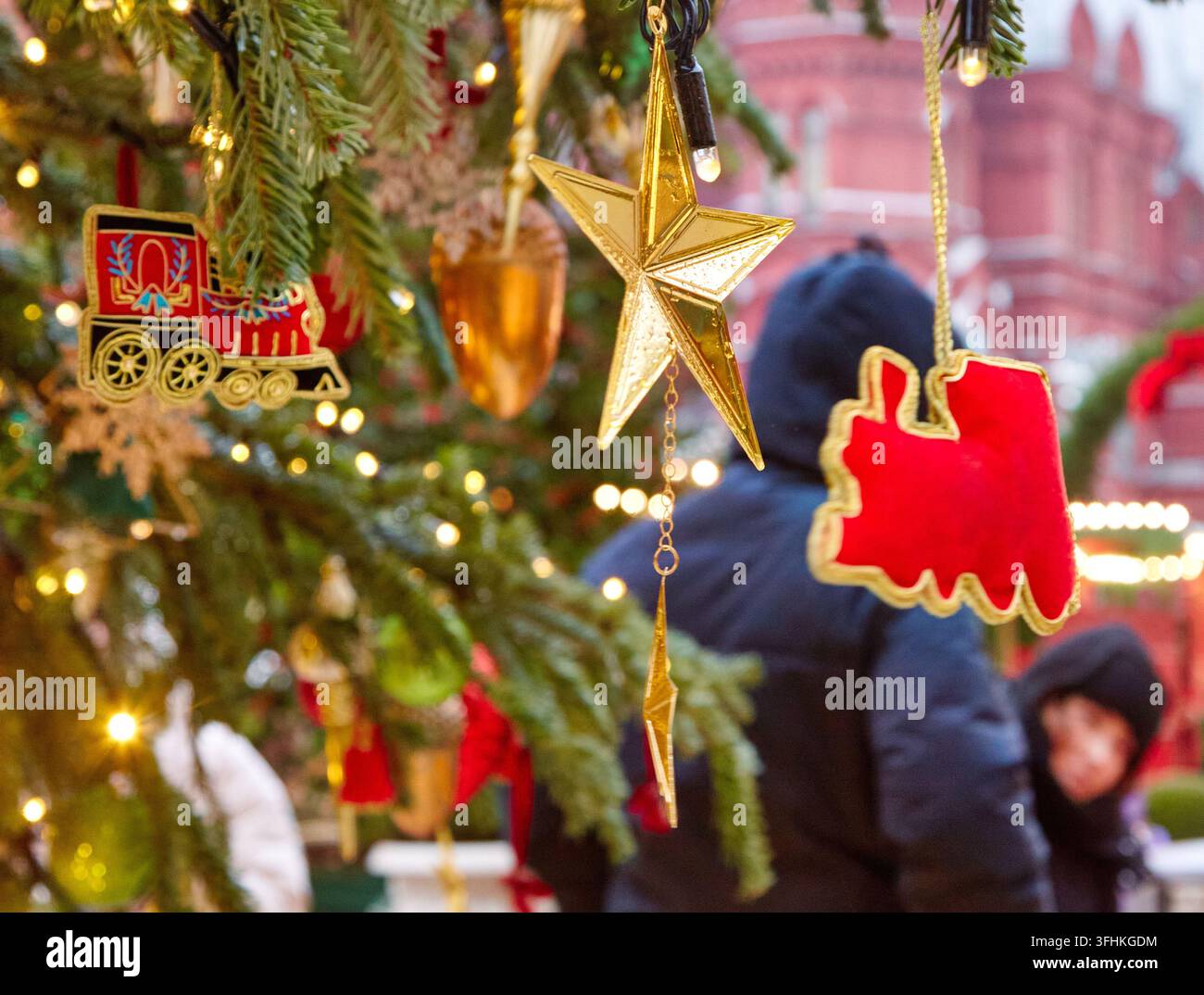 Weihnachtsbaum geschmückt mit einem Goldstern und verschiedenen Ornamenten, darunter eine Spielzeugbahn, beleuchtet von Lichtern in einer festlichen Umgebung Stockfoto