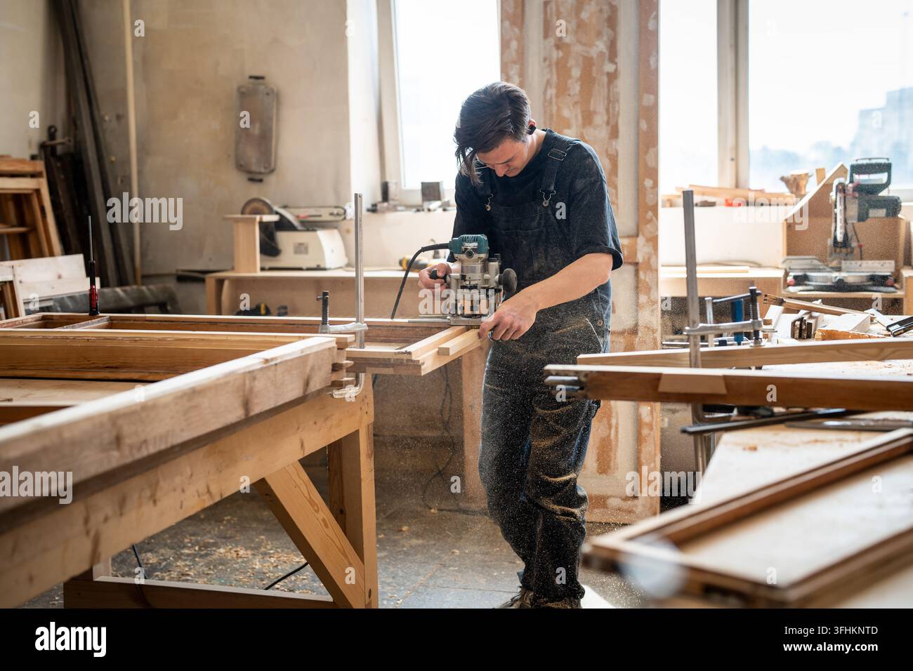 Fleißiger Handwerker in der Holzwerkstatt arbeitet mit einer elektrischen Handfräse und schneidet Holz ab. Stockfoto