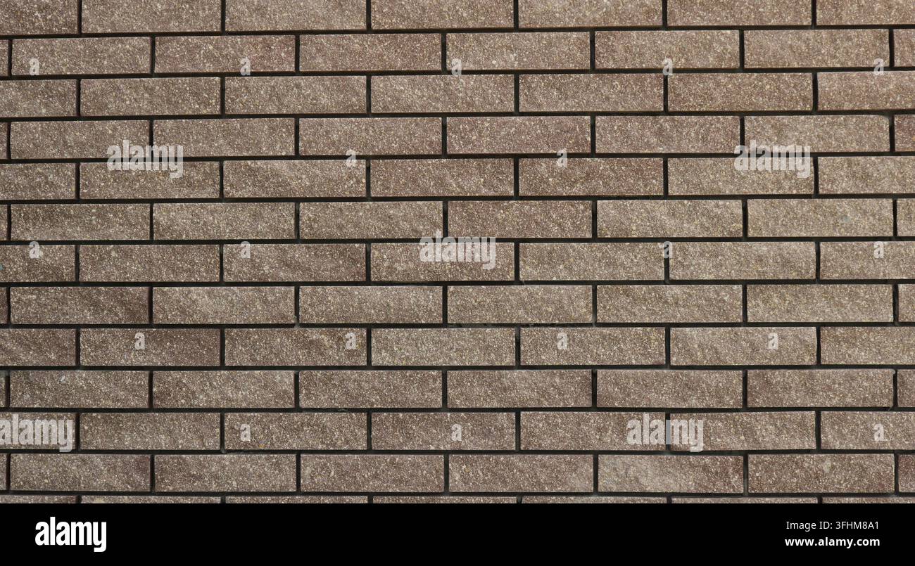 Eine Wand aus braunen Zierziegeln; glatte Fliesenoberfläche mit Ziegeloptik und sauberen Fugen. Verwendet für Innenverkleidungen und Gebäudefassaden. Stockfoto
