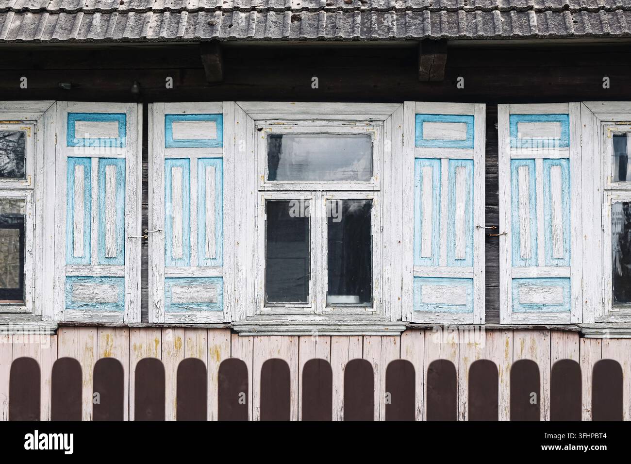 Alte Holzhausfenster mit blauen Fensterläden und verwitterter Fassade. Architekturhintergrund für ländliches Erbe, Volksdesign und traditionelle Häuser. Stockfoto