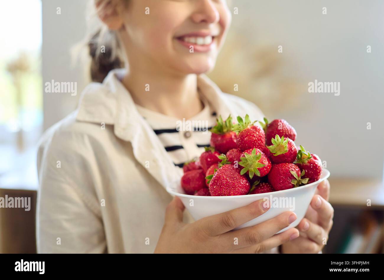 Nahaufnahme eines lächelnden Kindes, das eine Schüssel voller reifer Erdbeeren als gesunden Snack zu Hause hält Stockfoto