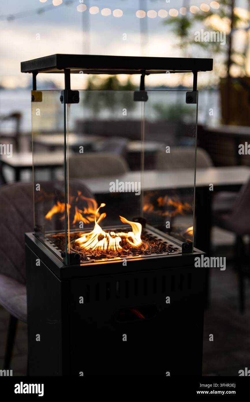 Moderner Gas-Kamin im Freien mit Flammen in einer Glasbox für den Komfort der Gäste auf der Restaurantterrasse. Stockfoto