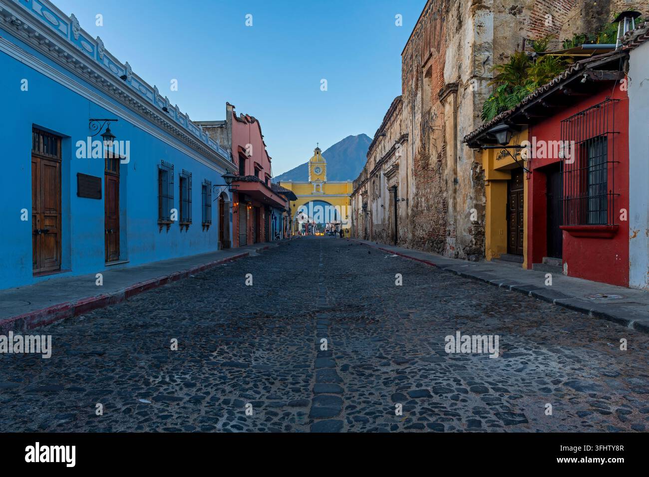 Hauptstraße von Antigua vor Sonnenaufgang mit dem Bogen der Santa Catalina und dem Agua-Vulkan, Guatemala. Stockfoto