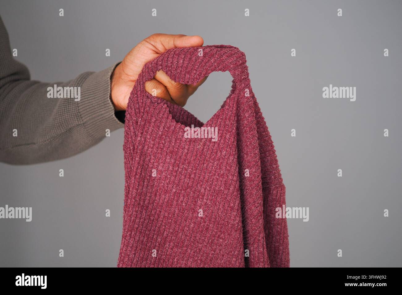 Hand, die ein Kleidungsstück mit einem Loch darin hält Stockfoto