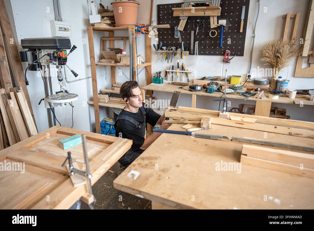Begabter Tischler renoviert altes Holzbrett, schneidet beschädigtes Stück mit Handsäge ab. Stockfoto