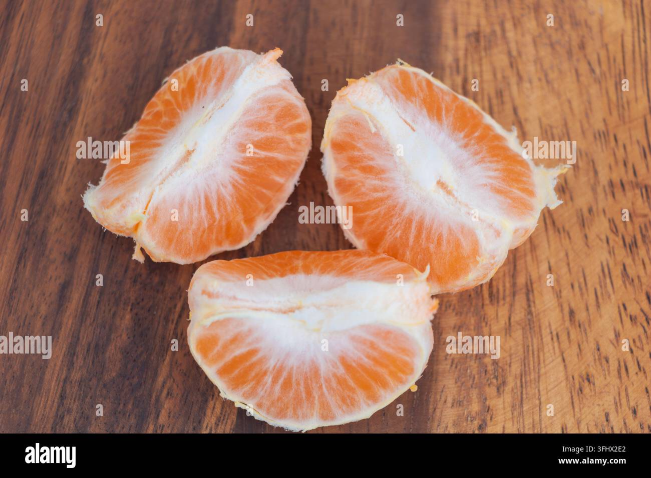 Geschälte Mandarinenstücke mit hellorangen Segmenten und weißem Fruchtfleisch auf einer Holzoberfläche. Stockfoto