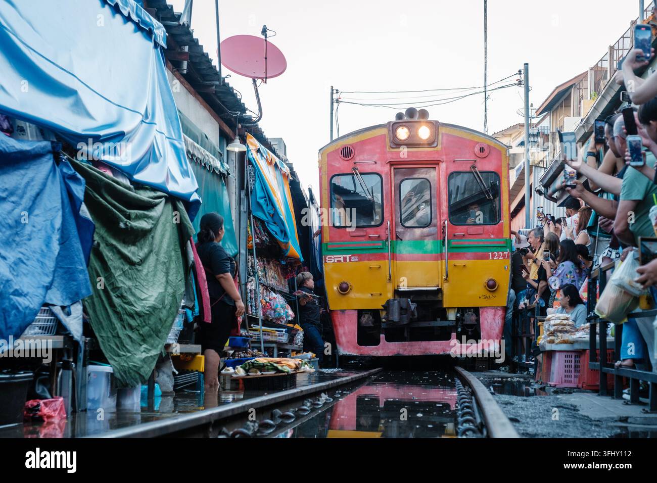 Maeklong Railway Market, Thailand, am 5. Dezember 2025 ziehen Händler schnell zur Seite, während ein Zug durch den belebten Markt fährt. Eine fesselnde Szene Stockfoto