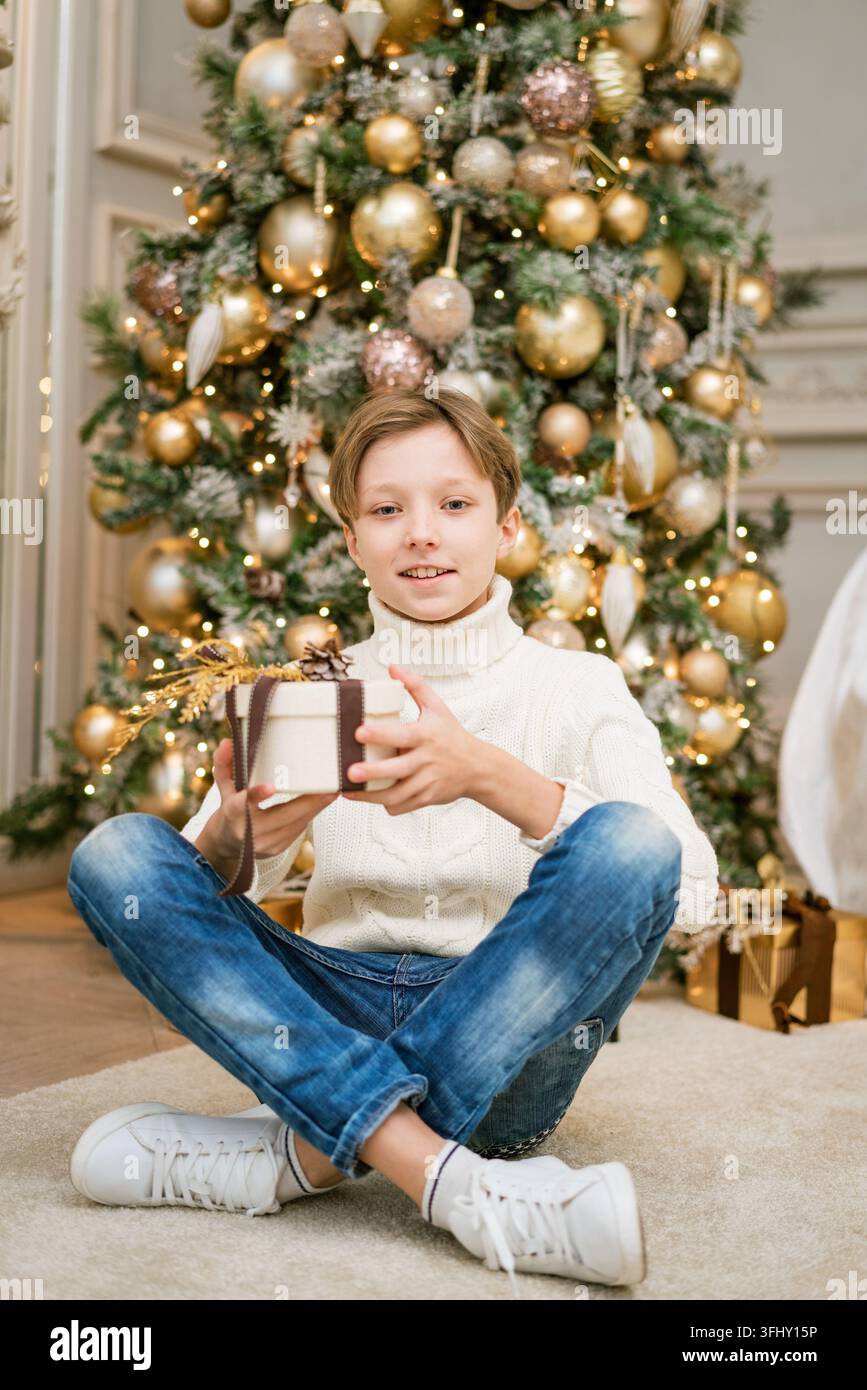 Süßer Junge sitzt neben dem Weihnachtsbaum mit Geschenken Stockfoto