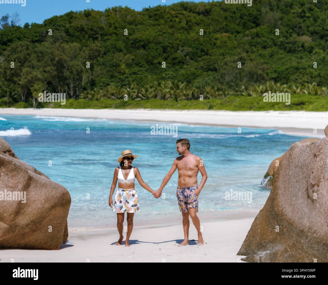 Ein paar Spaziergänge Hand in Hand entlang der unberührten Küste von Anse Cocos Beach, La Digue, Seychellen. Stockfoto