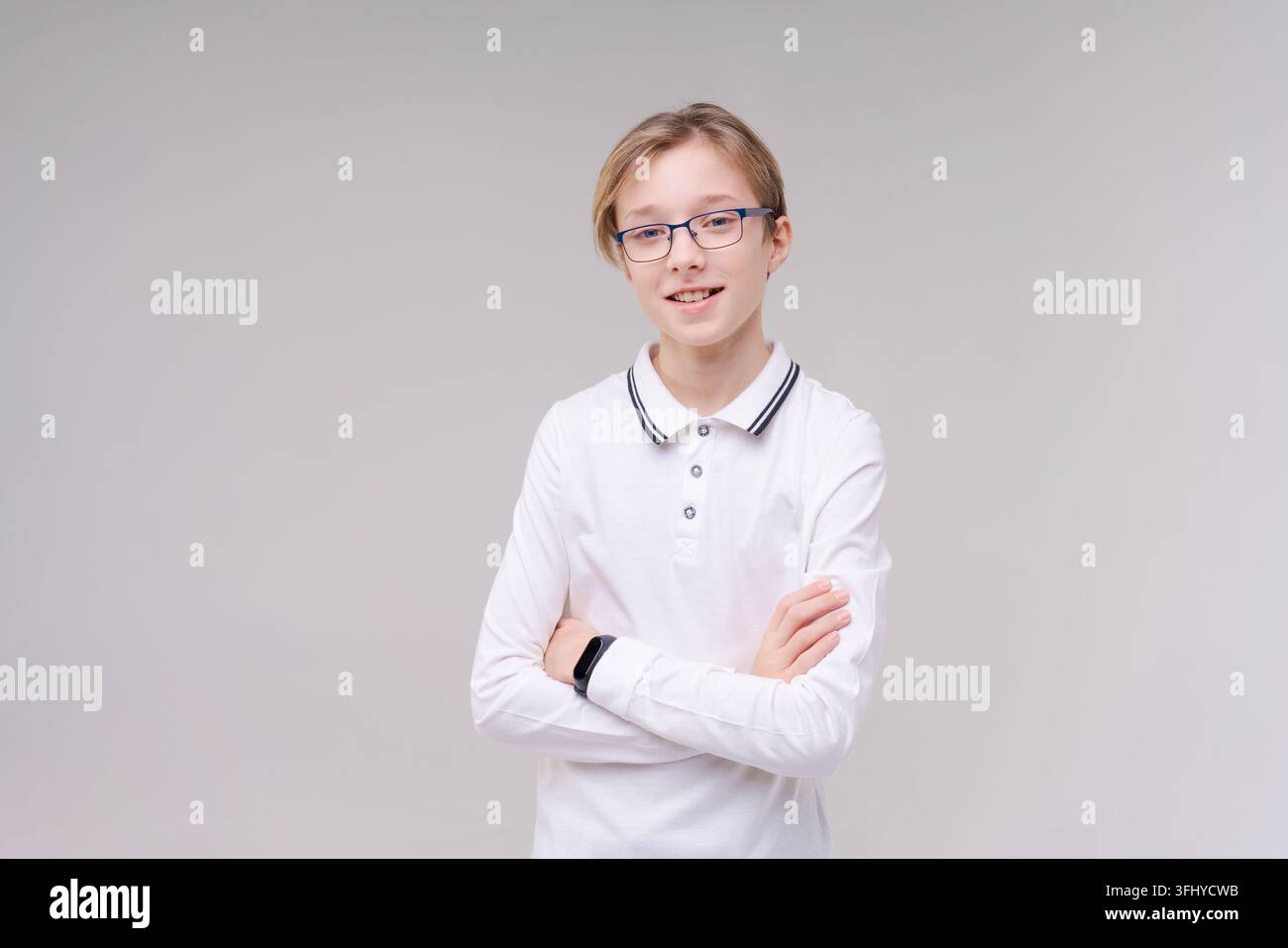 Zuckender kaukasischer Junge, zweifelende zuckende Schultern, Schuljunge, Teenager mit Brille in einem weißen T-Shirt. Der Junge wählt auf einem grauen Hintergrund. Stockfoto