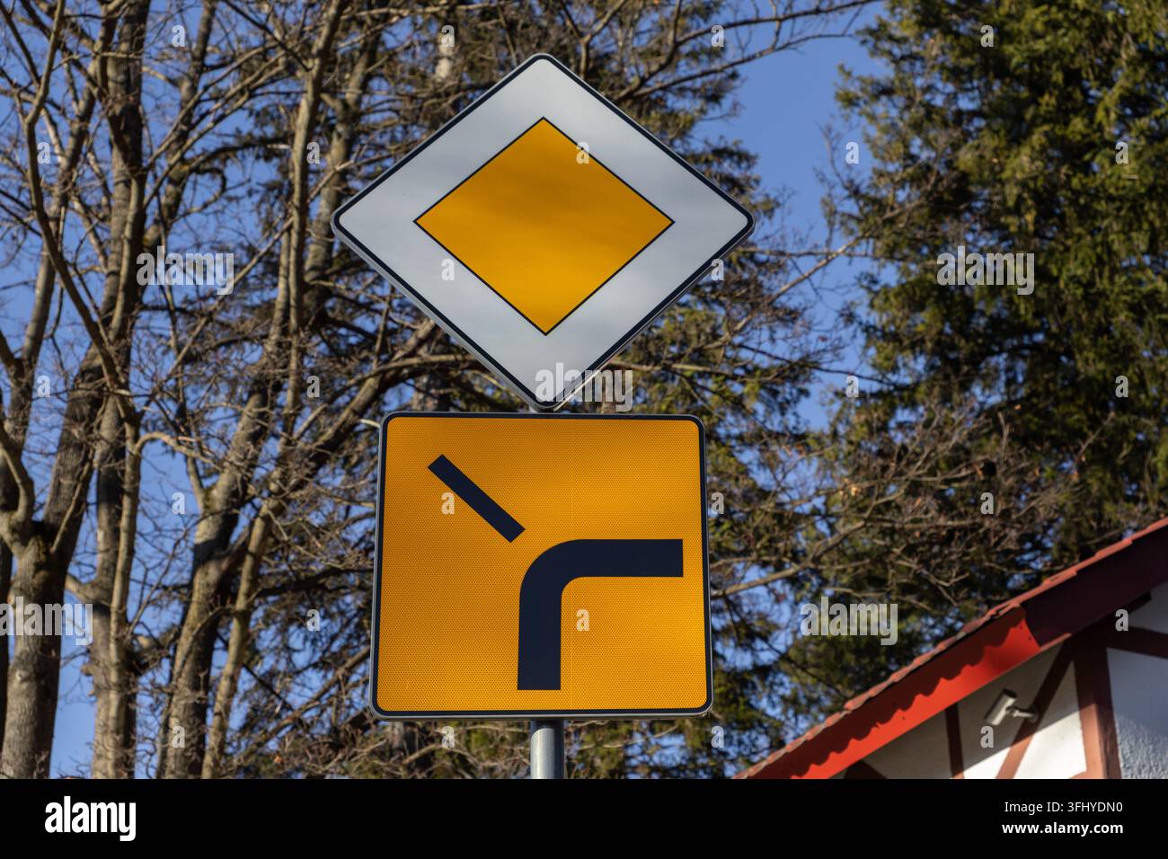 Standard-Trafikschilder, die Vorfahrt und Straßenkrümmung anzeigen, sind im Freien installiert und bieten klare Navigations- und Sicherheitsinformationen für Autofahrer Stockfoto