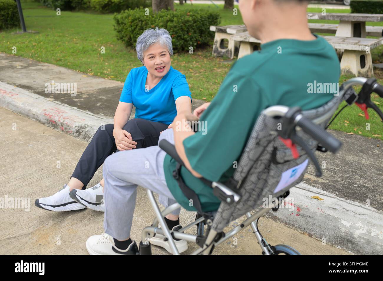 Seniorin spricht mit einem Mann im Rollstuhl in einem Park und schafft eine warme und unterstützende Atmosphäre Stockfoto
