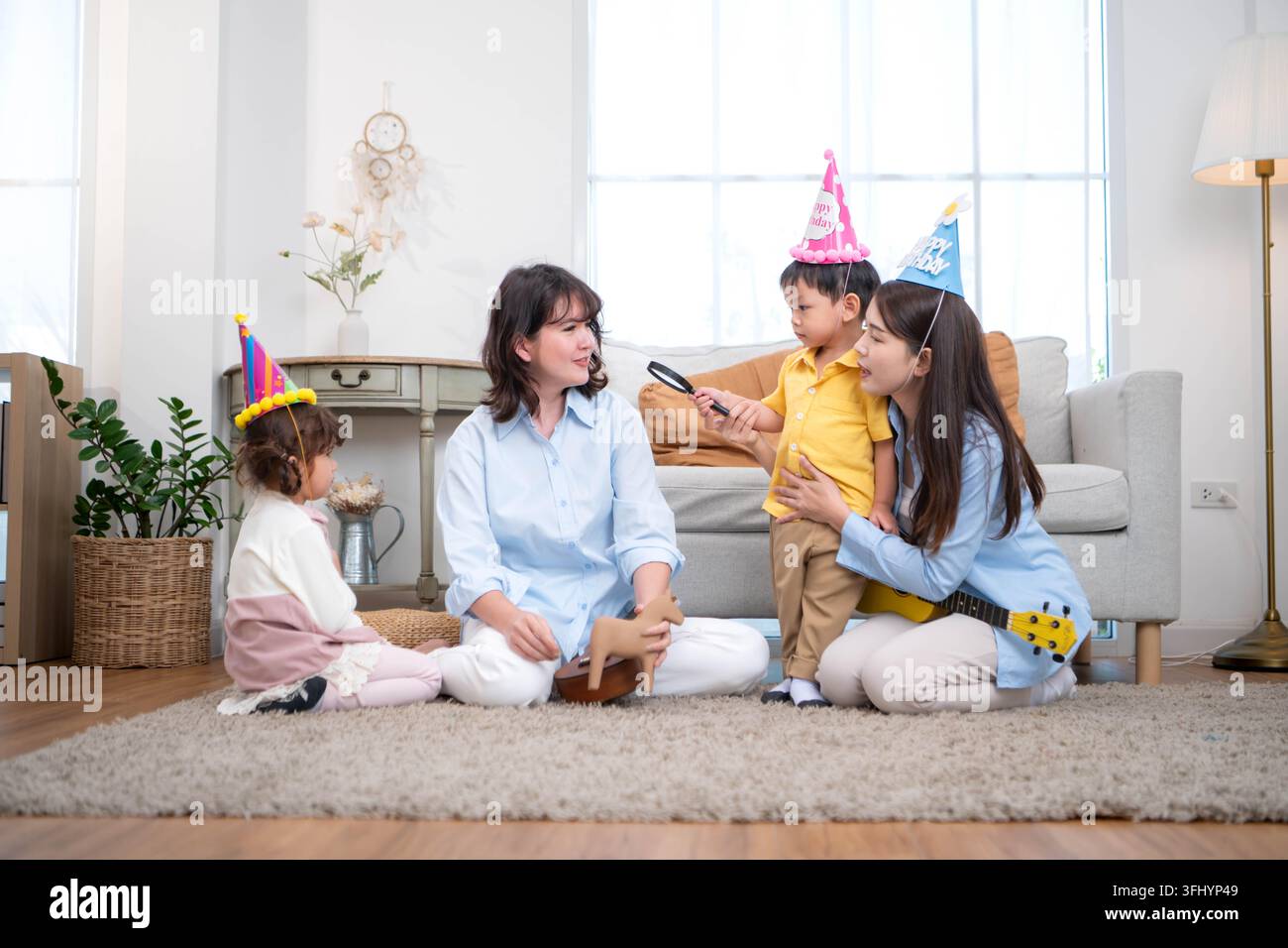 Mutter und Kinder, die sich in einer warmen häuslichen Aktivität beschäftigen, wobei ein Kind eine Lupe benutzt, um Objekte zu erkunden, was das frühe Lernen und Denken fördert Stockfoto