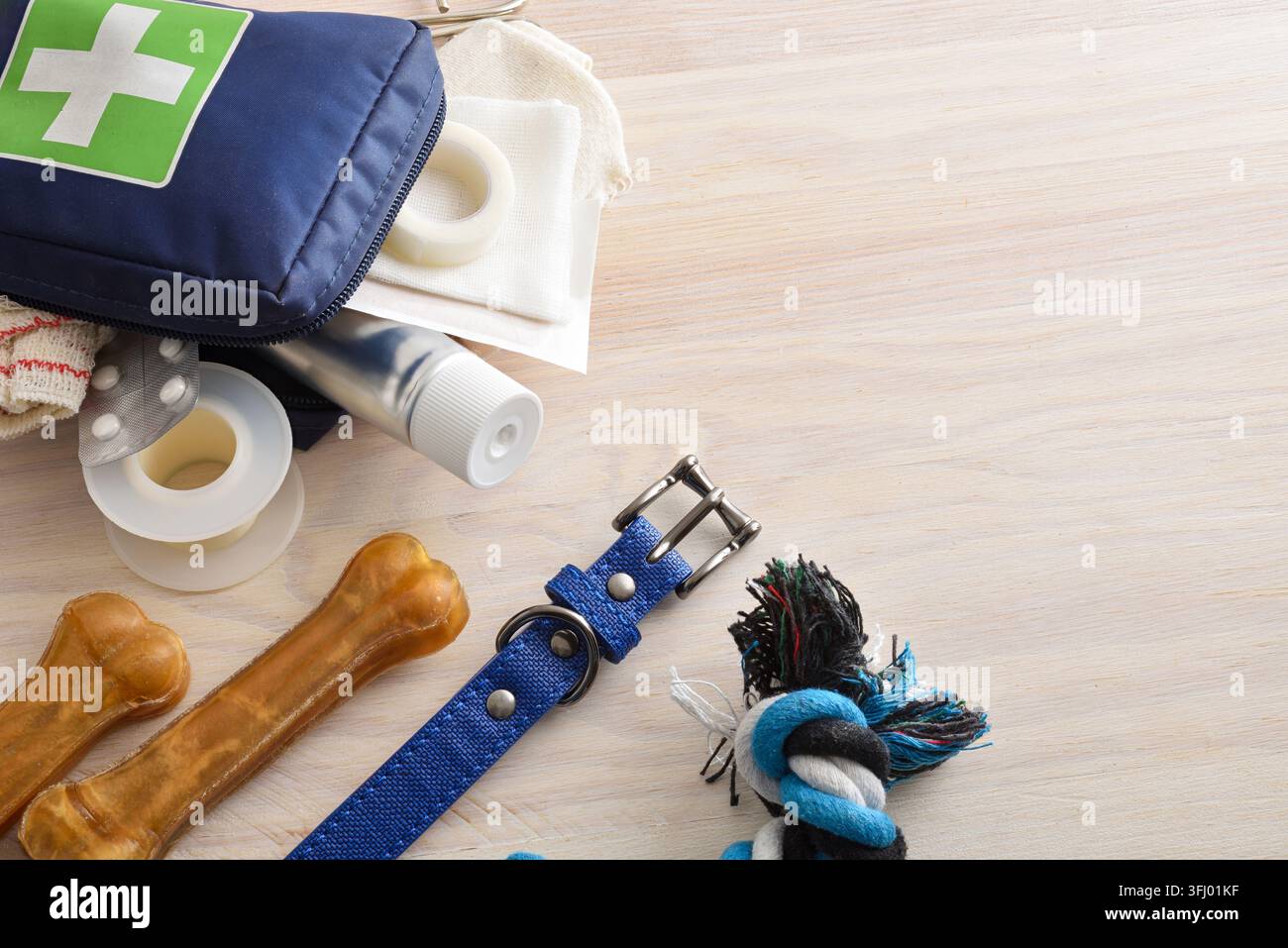 Nahaufnahme eines Hundehalsbandes, eines Seilspielzeugs, Kauknöchel und eines Teils eines Erste-Hilfe-Sets für Haustiere mit medizinischen Hilfsmitteln auf einem hellen Holztisch. Stockfoto