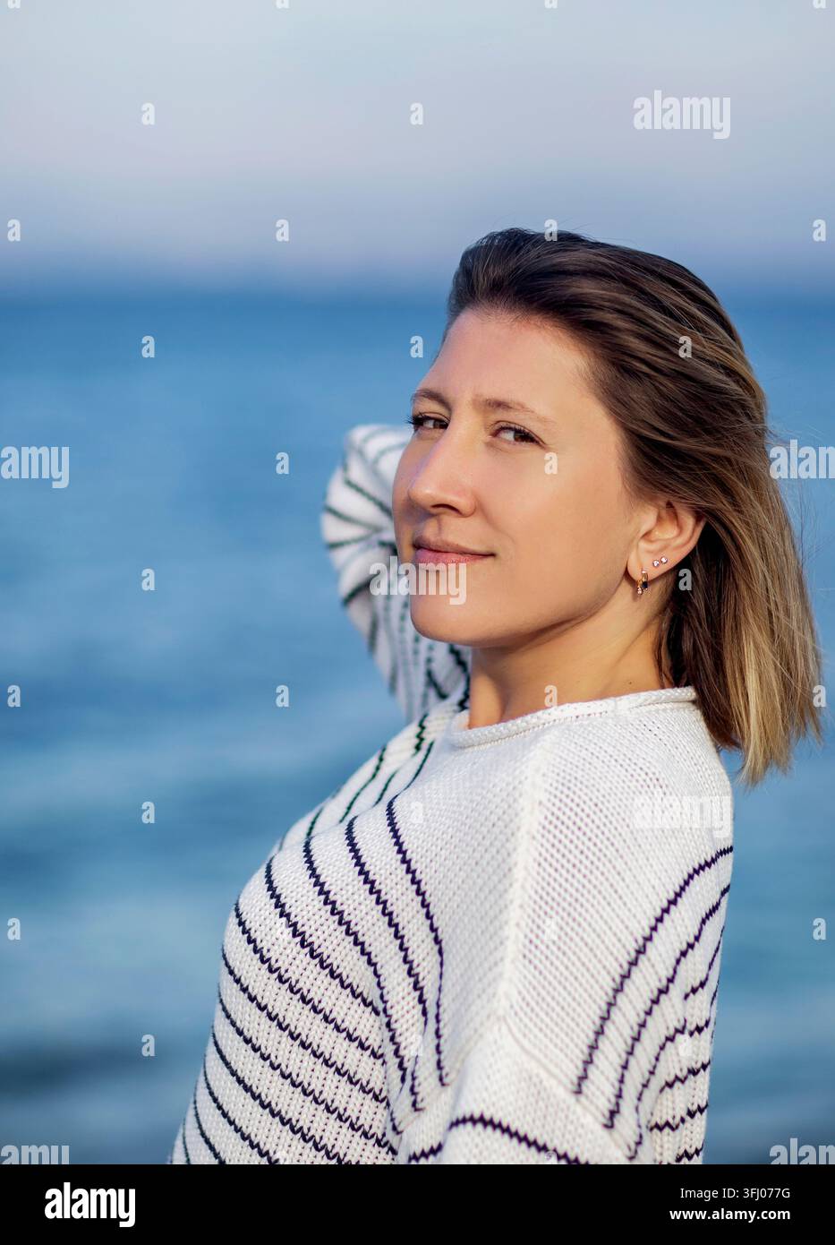 Schöne Frau in gestreiftem Pullover, die über ihre Schulter schaut Stockfoto