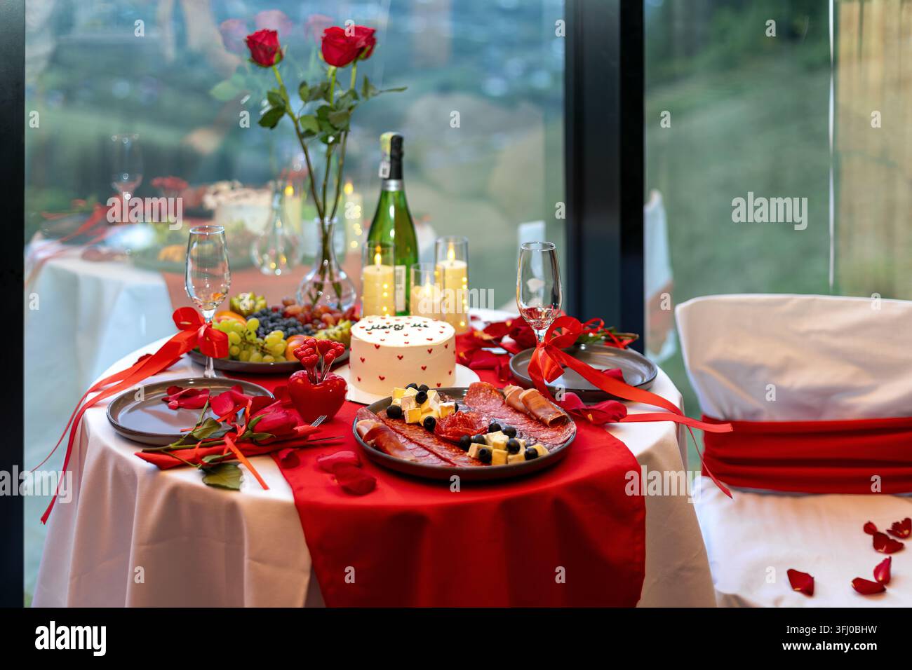Romantisches Esstisch mit Rosen, Kuchen und Champagner. Romantische Tischgestaltung mit roten Rosen, Kuchen, Champagner, Kerzen, Obst und Wurstwaren arrangiert Stockfoto