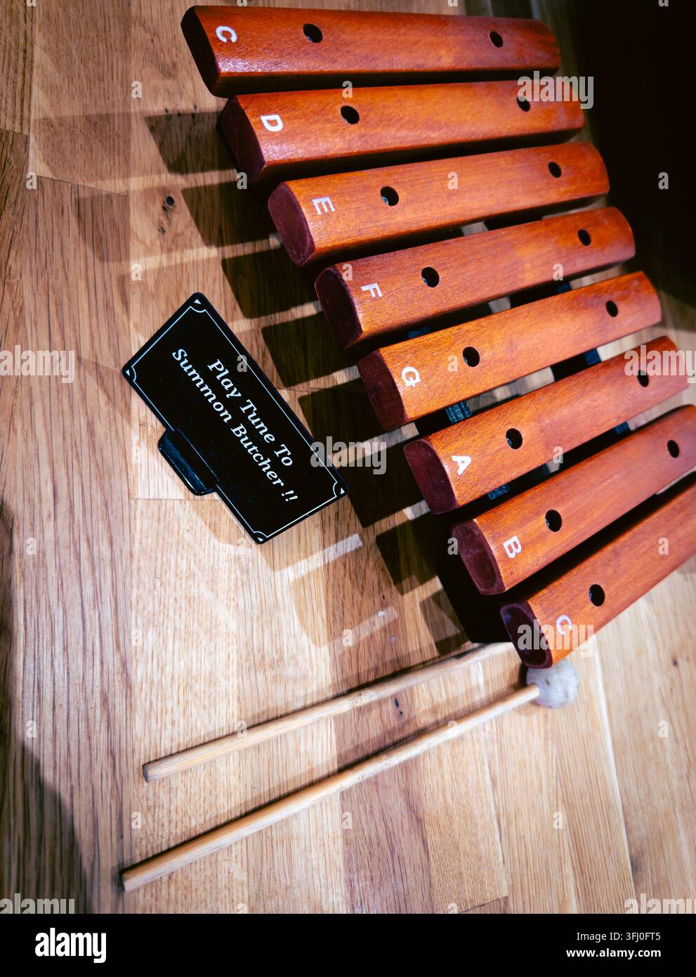 Holzglocken mit Musiknoten beschriftet und zwei Schlägern in einem Bauernladen, mit einem Schild, das Kunden einlädt, sie zu spielen, um den Metzger zu rufen Stockfoto
