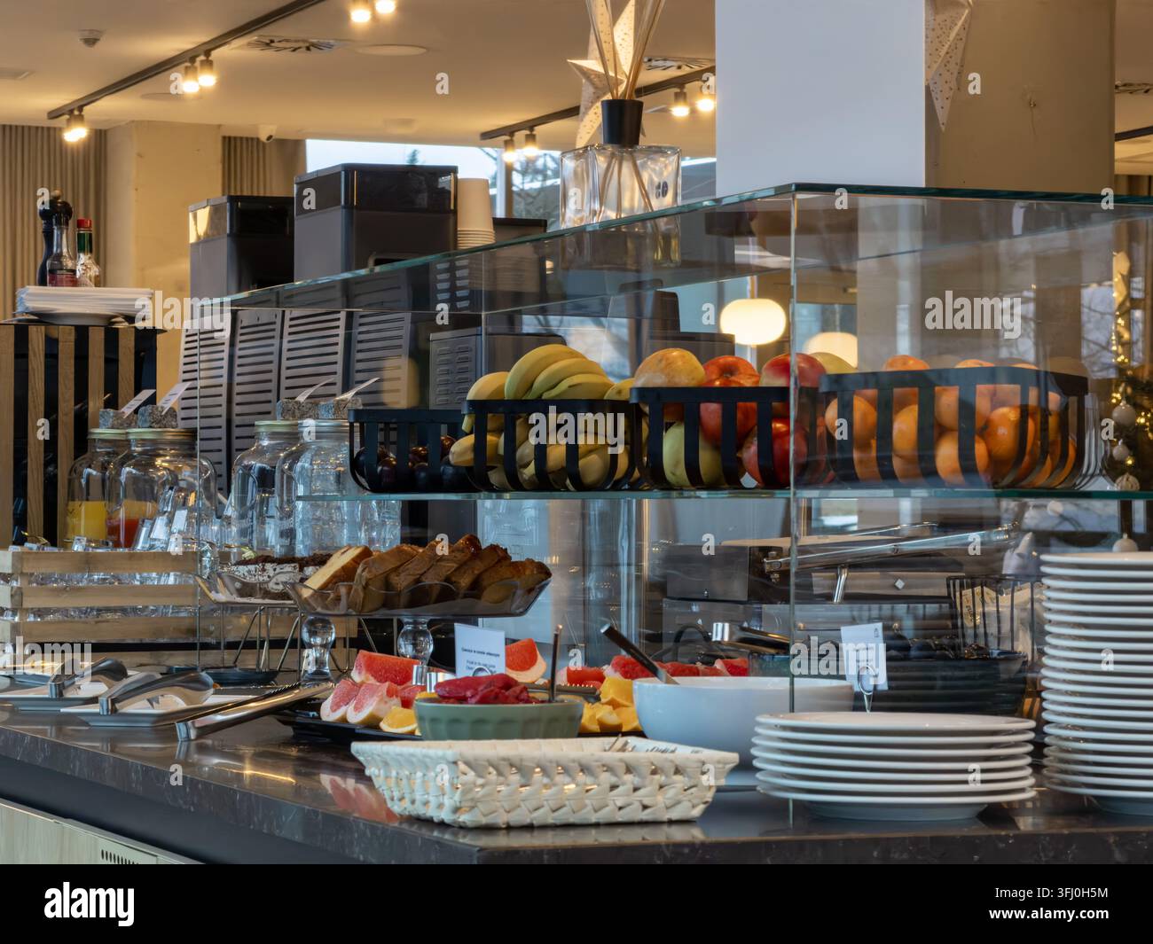 Gesunde Frühstücksauswahl mit reifen Bananen, Orangen und geschnittenem Brot in einer Glasvitrine, die einen gut organisierten Selbstbedienungsbereich präsentiert Stockfoto