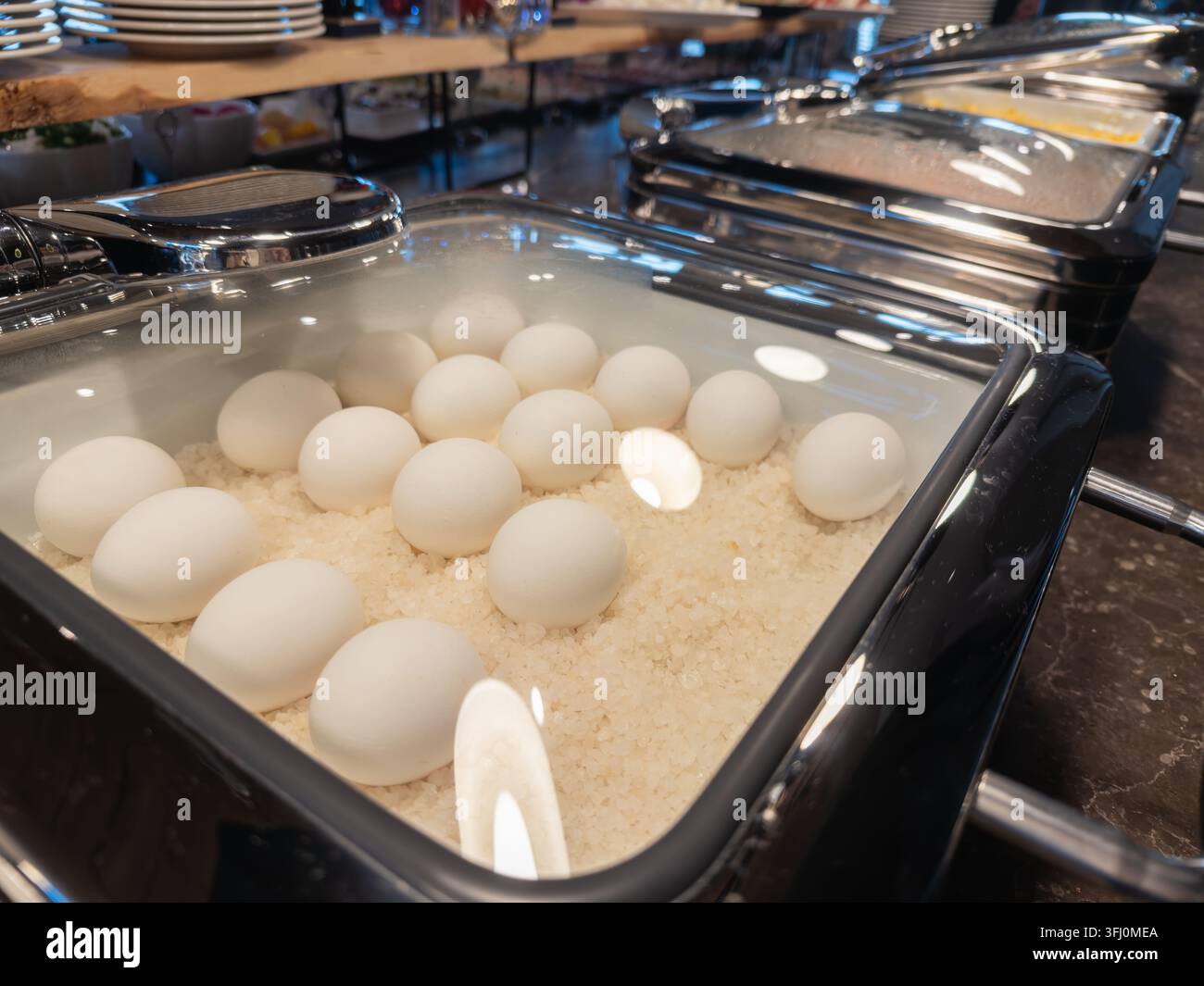 Gekochte Eier auf einem Bett aus Salz in einer Rechaudschale an einem Hotel-Frühstücksbuffet, die saubere Präsentation und die appetitliche Auslage typisch einfangen Stockfoto