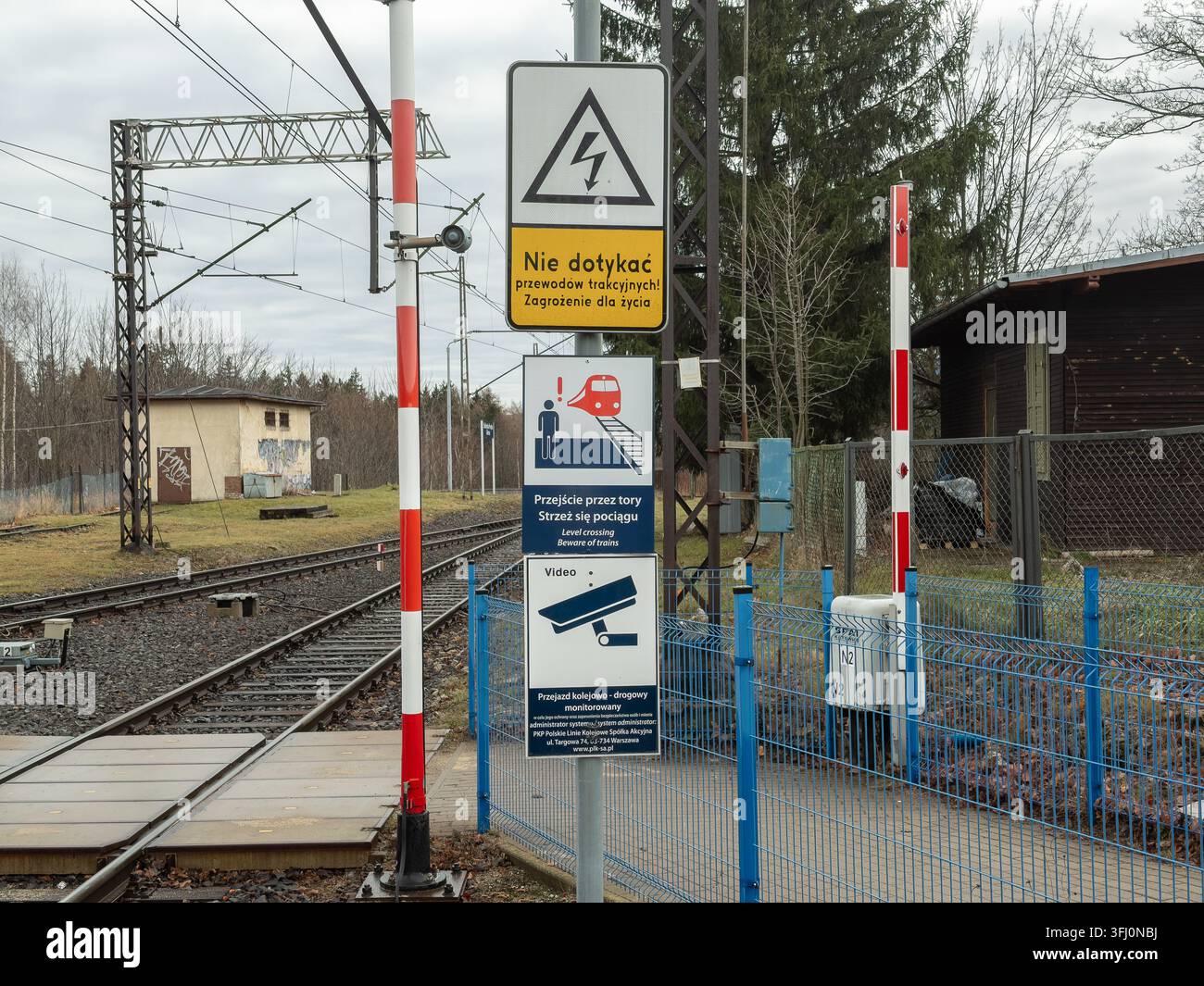 Szklarska Poręba, Polen – 21. Dezember 2025: Sicherheitsschild an einem Bahnübergang warnt vor Hochspannung und Überwachungsmonitoren Stockfoto
