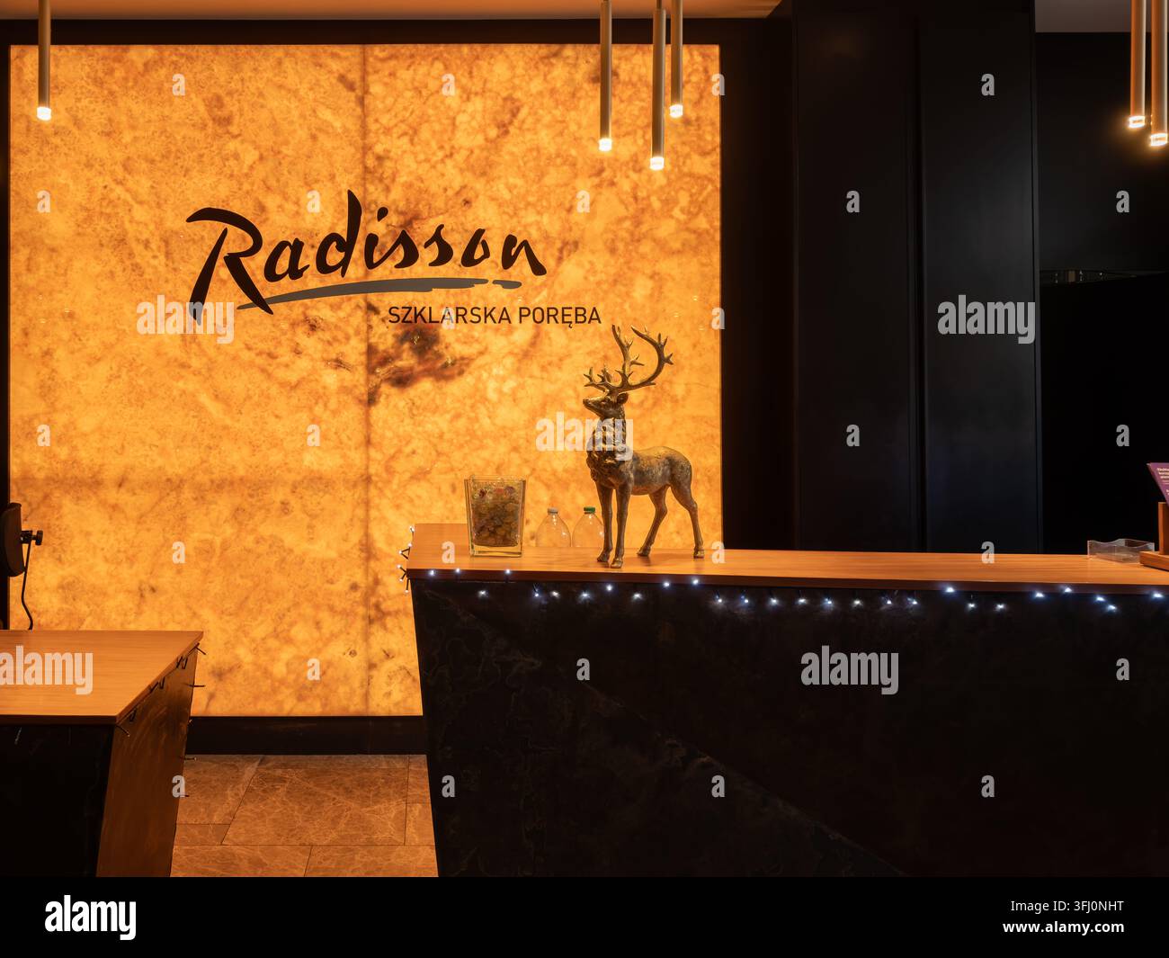 Szklarska Poręba, Polen – 21. Dezember 2025: Die Lobby des Radisson Szklarska Poręba verfügt über einen Empfangstresen, eine leuchtende Onyxwand und ein Hirsch-Ornament fo Stockfoto