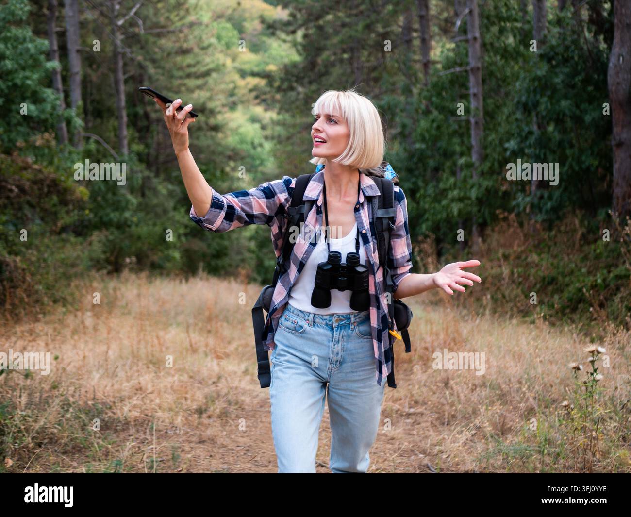 Verärgerte und verirrte Wandererin versucht, ein Signal für ihr Smartphone zu finden, während sie im Wald wandert. Sie wirkt verwirrt über den Weg. Stockfoto