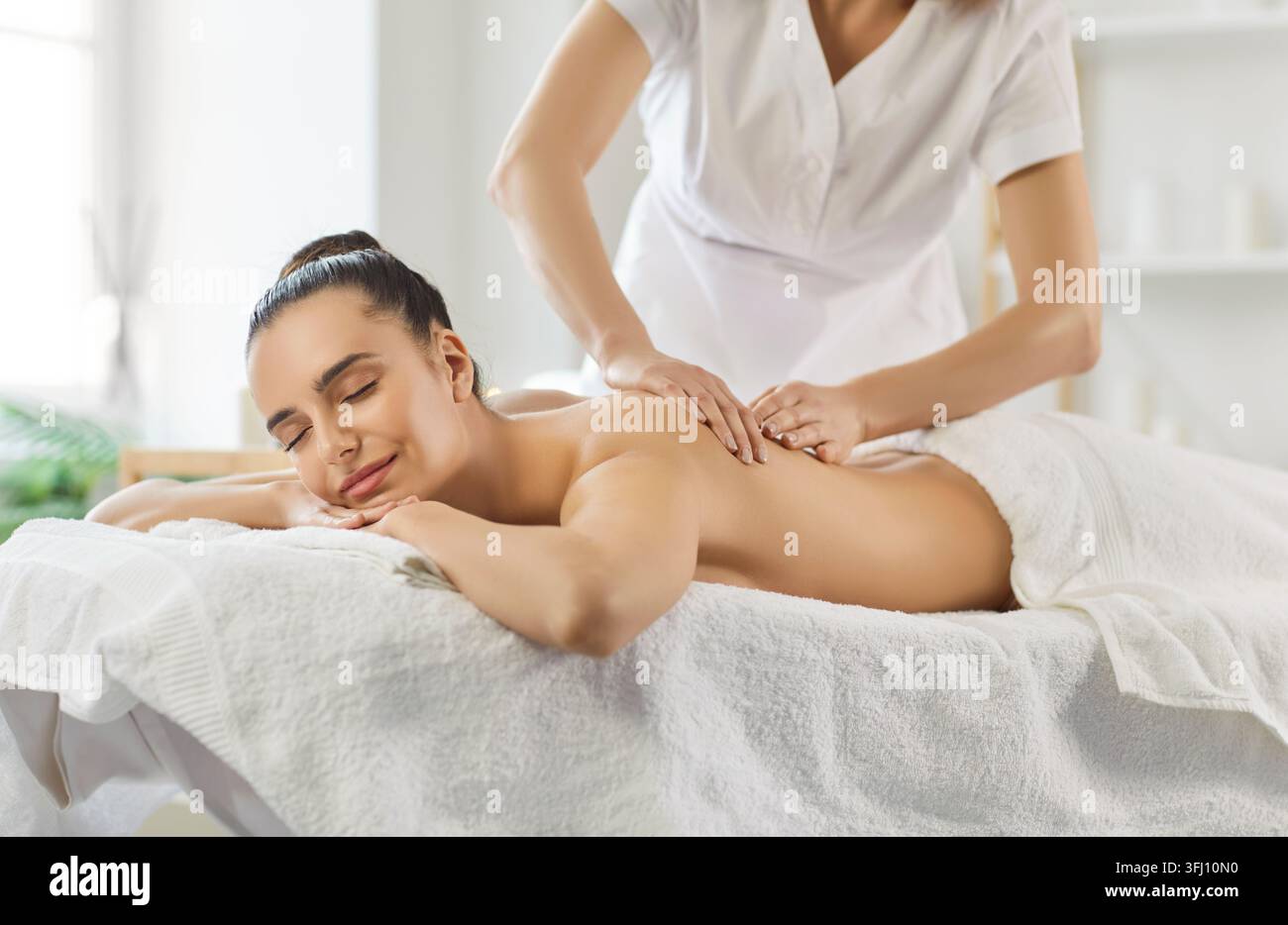 Lächelnde junge Frau mit geschlossenen Augen genießt eine entspannende Rückenmassage in einem Wellness-Spa-Zentrum. Stockfoto