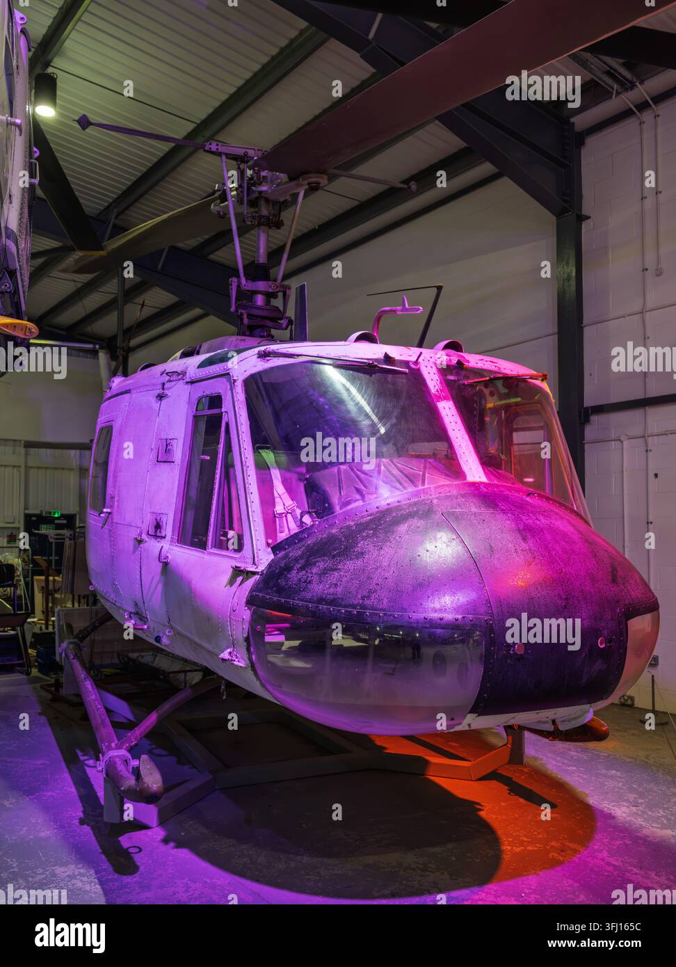 Die Nasen- und Kabinensektion eines historischen Bell UH-1 Iroquois Huey-Hubschraubers in einer Innenausstellung unter purpurfarber Beleuchtung im Army Flying Museum, UK Stockfoto