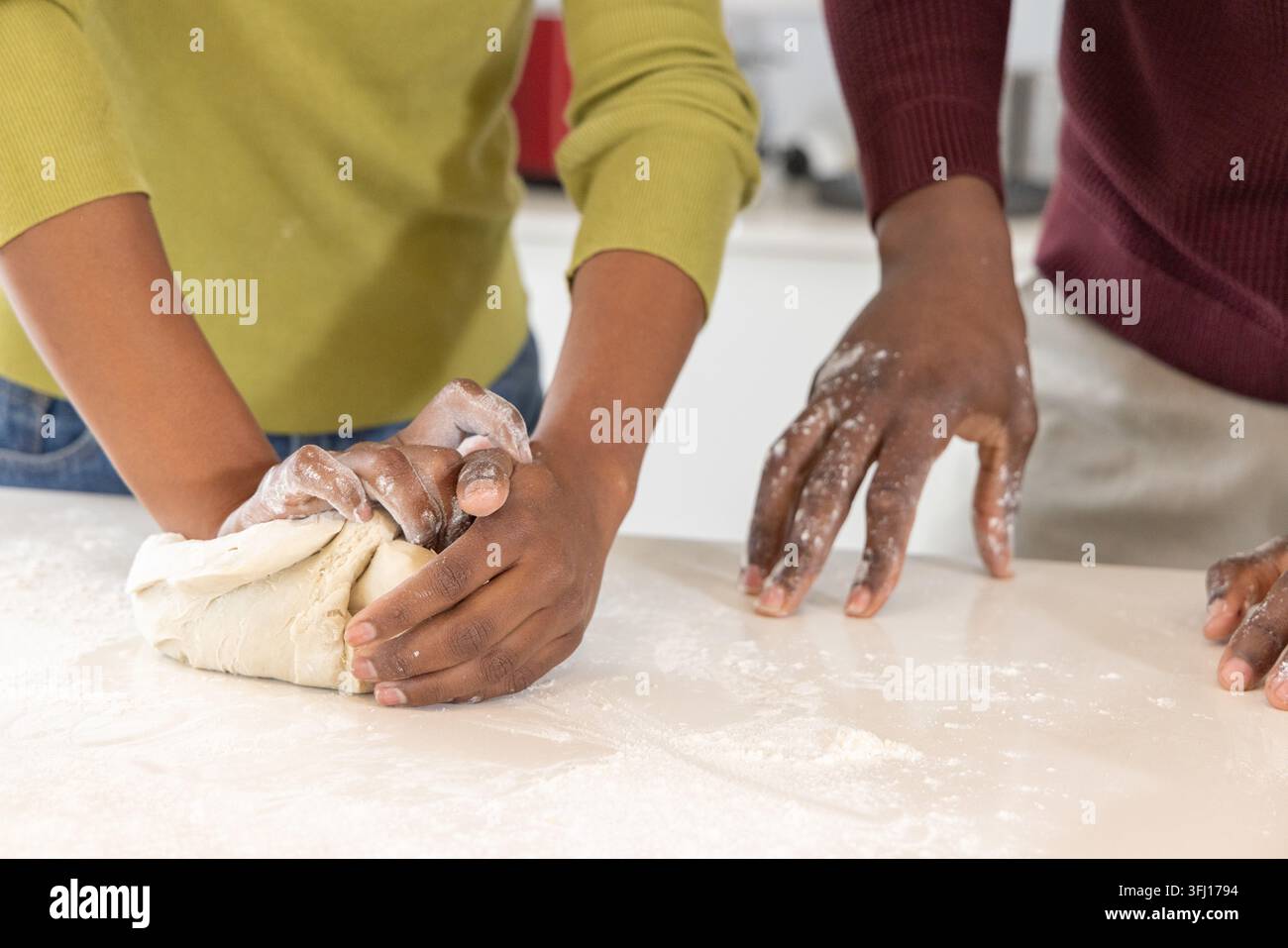 Afroamerikanische Freunde kneten Teigkugel mit Mehl auf weißer Theke, tragen lange Ärmel. Hände, Backen, Küche, Zusammenarbeit, Brot, Rusti Stockfoto
