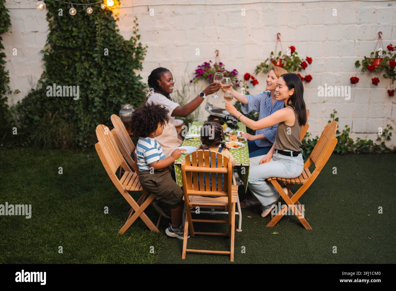 Bei einem festlichen Abendessen im Freien lächeln und trinken verschiedene Familien und Freunde Stockfoto