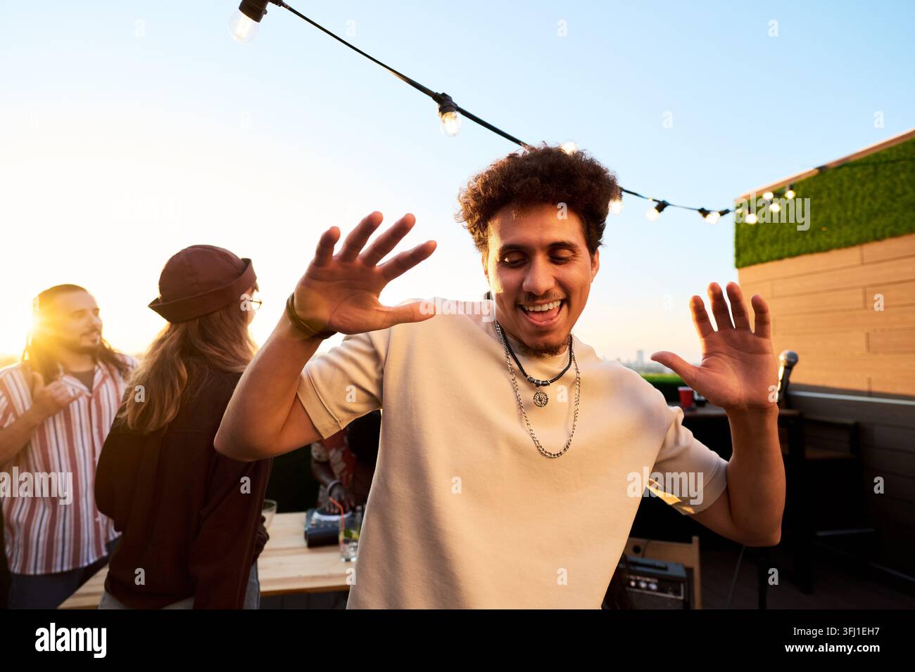 Fröhlicher Mann tanzt auf einer Outdoor-Dachparty während des Sonnenuntergangs Stockfoto