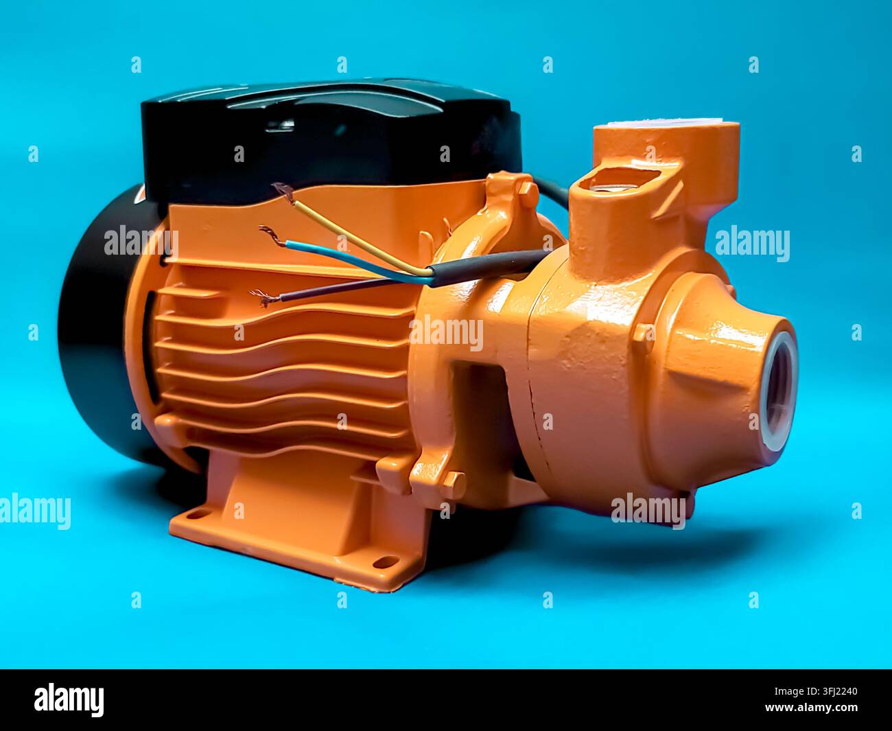 Orange Dynamowasserpumpe mit freiliegenden Drähten, isoliert auf blauem Hintergrund. Stockfoto
