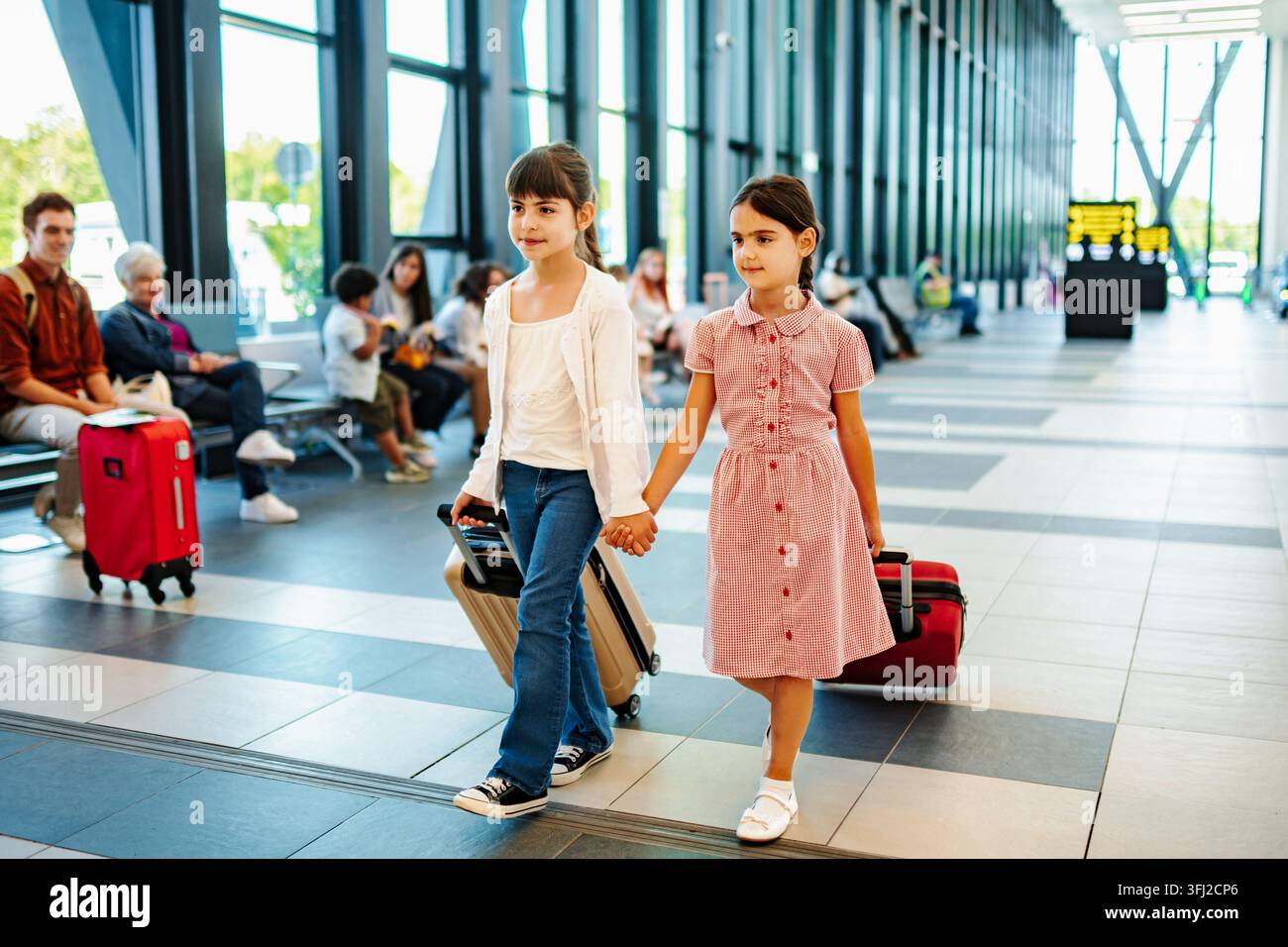 Schwestern gehen am Flughafen und ziehen Rollgepäck hinter sich her Stockfoto