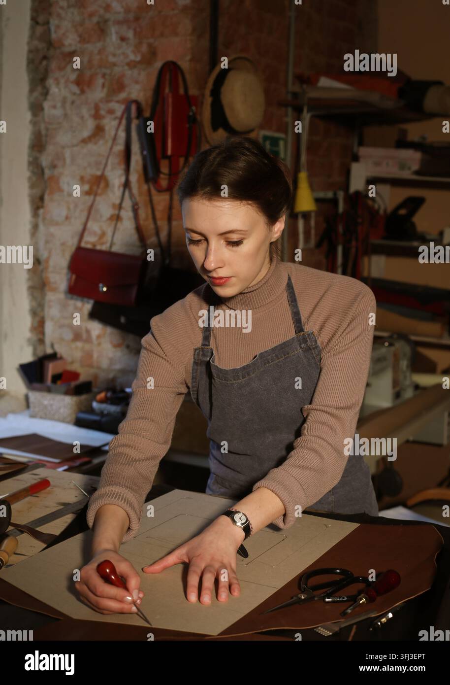 Junge Frau arbeitet in einem Taschenstudio, schneidet Details aus Stockfoto