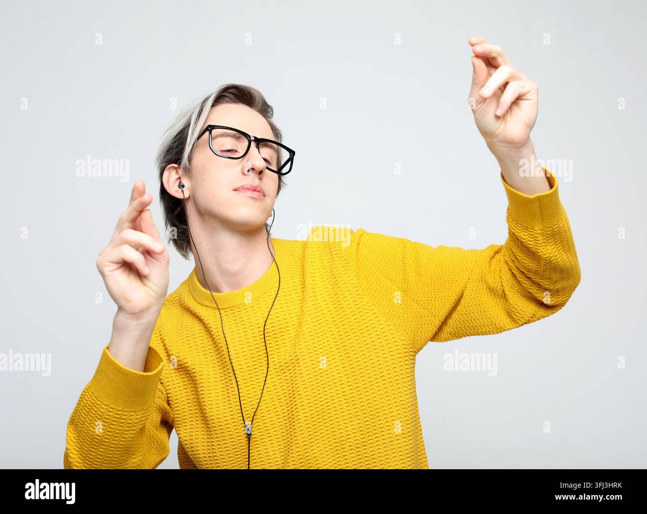 Stylischer modischer junger Mann trägt einen gelben Pullover mit Kopfhörern und tanzt zur Musik Stockfoto