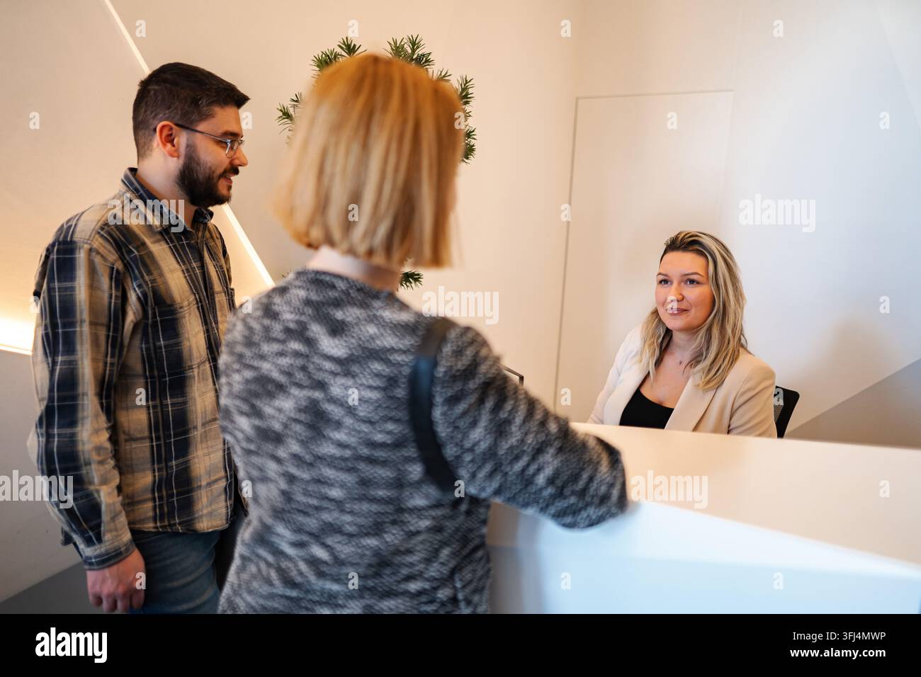Klienten interagieren mit der Rezeptionistin am modernen Empfangstisch im Büro Stockfoto
