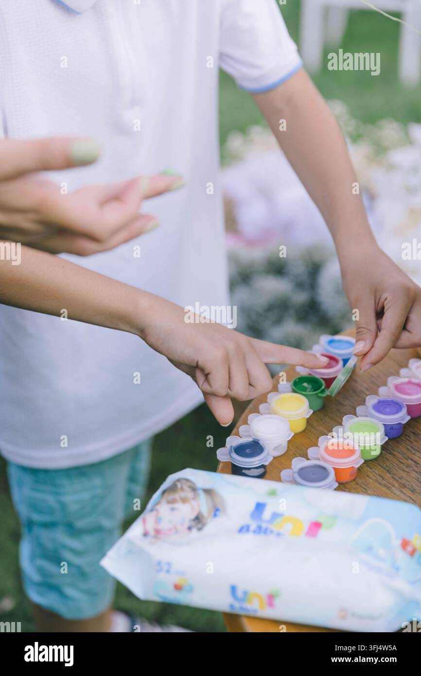 Nahaufnahme von Händen, die farbenfrohe Farben aus einem Kunstset während einer kreativen Aktivität im Freien auswählen. Konzept der Kreativität, künstlerischen Ausdrucksweise. Stockfoto
