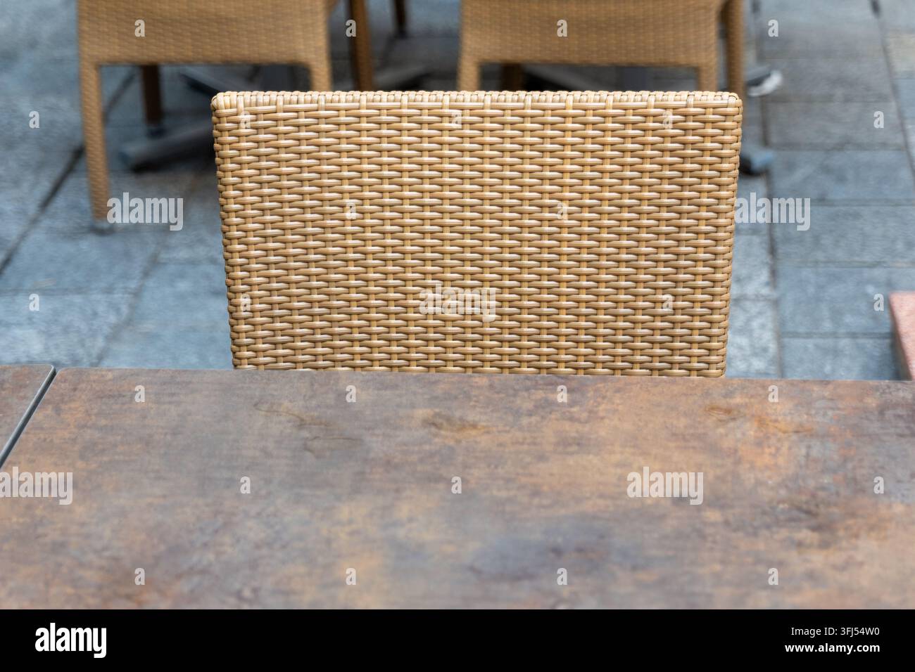Ein leerer Korbstuhl steht hinter einem verwitterten Tisch auf einer Außenterrasse eines Cafés. Stockfoto