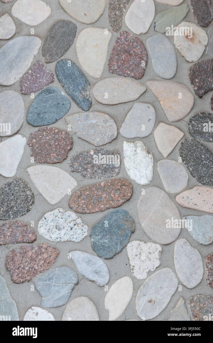 Eleganter Kieselhintergrund mit Flusskieseln als dekoratives Wanddesign in Beton. Moderne Wohnkultur mit natürlichen bunten Kieselsteinen als Außendekoration für Wände Stockfoto