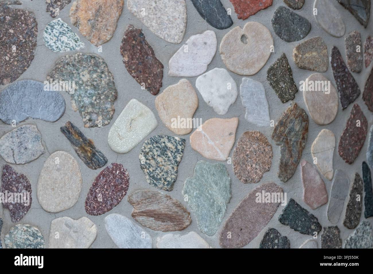Eleganter Kieselhintergrund mit Flusskieseln als dekoratives Wanddesign in Beton. Moderne Wohnkultur mit natürlichen bunten Kieselsteinen als Außendekoration für Wände Stockfoto
