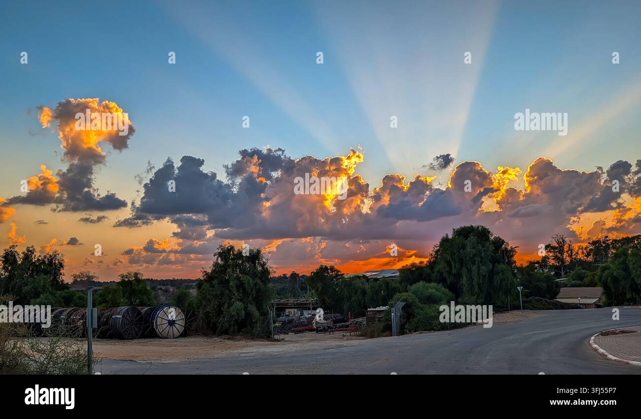 Eine beeindruckende, feurige Sonnenunterganglandschaft am Eingang zu Ruhama, Israel. Die untergehende Sonne sendet Strahlen hellen Lichts in den dunkler werdenden Himmel. Stockfoto