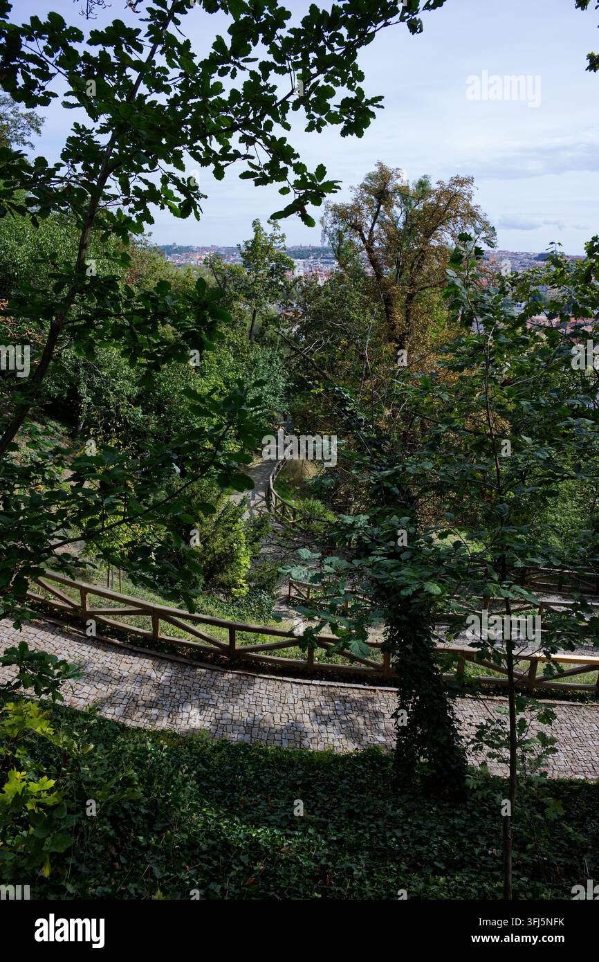 Enge Kopfsteinpflasterwege winden sich durch dichtes Grün mit einem teilweisen Blick auf Prag vom Kinsky-Garten aus. Stockfoto