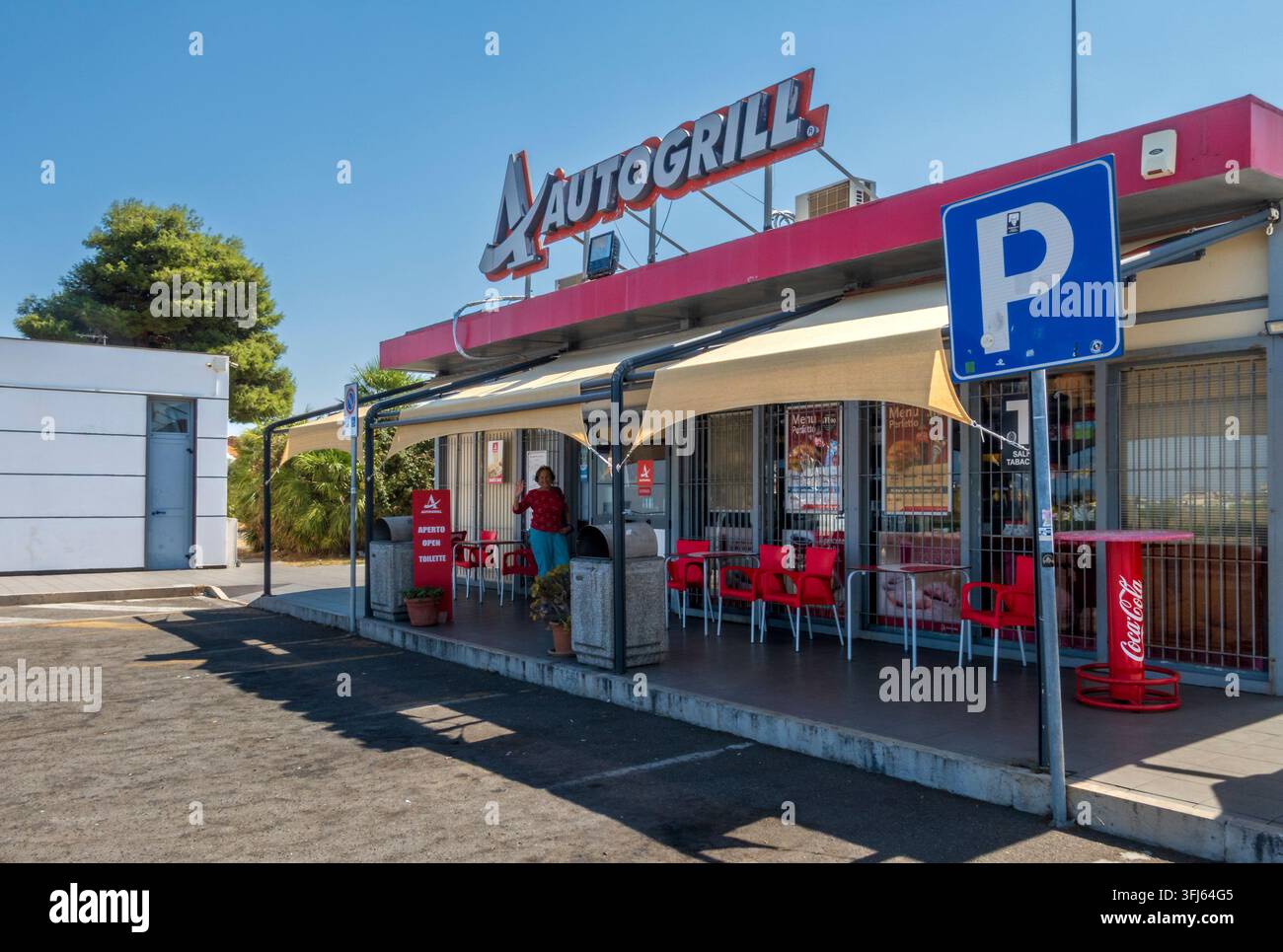 Milazzo - ME - IT - Sep 09, 2026: Autogrill-Servicebereich an der Autostrada, mit roten Sitzgelegenheiten im Freien, schattigen Markisen, Parkplatzschild, Schaufenstern und Stockfoto