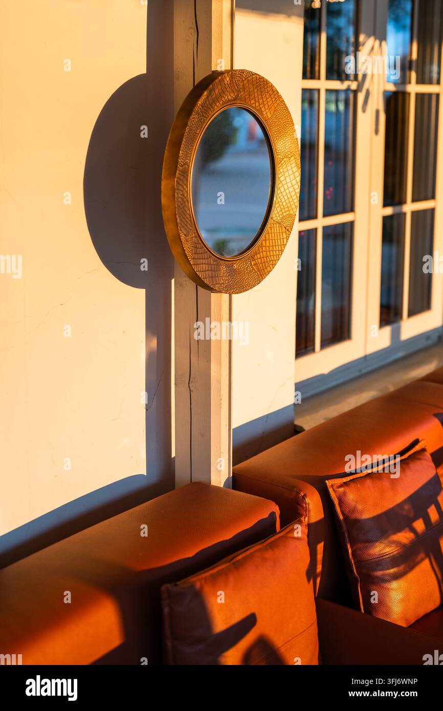 Details des Innenbereichs einer Straßencafé-Terrasse mit Sofas und einem runden Spiegel in Holzrahmen an der Wand. Stockfoto