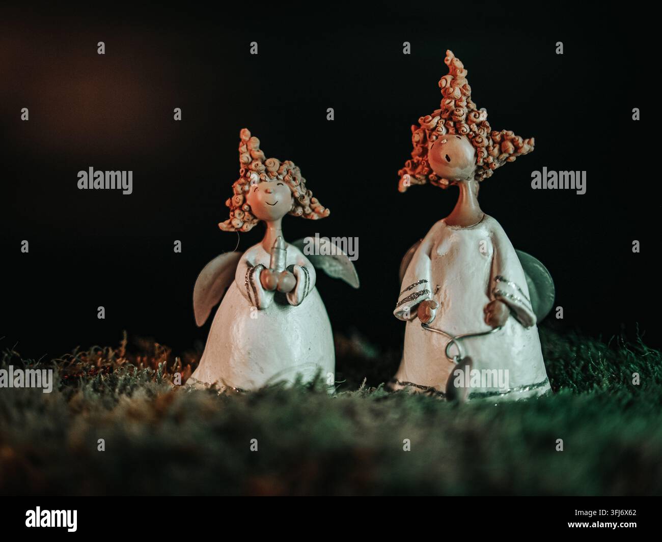 Zwei verspielte Engelsfiguren mit Flügeln und lockigem Haar, die vor einem dunklen Hintergrund in einem festlichen Stillleben ausgestellt sind. Stockfoto