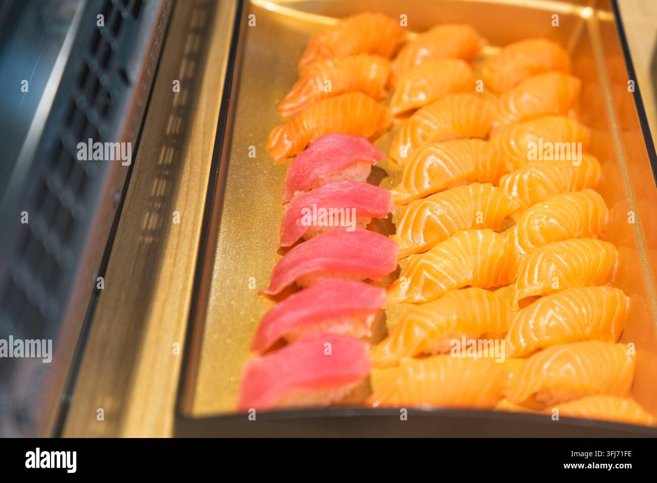 Japanisches Sushi-Esskonzept, Reihen von frischem Lachs- und Thunfisch-Nigiri, angeordnet auf einem goldenen Serviertablett in der Restauranttheke, repräsentierend authentisch Stockfoto